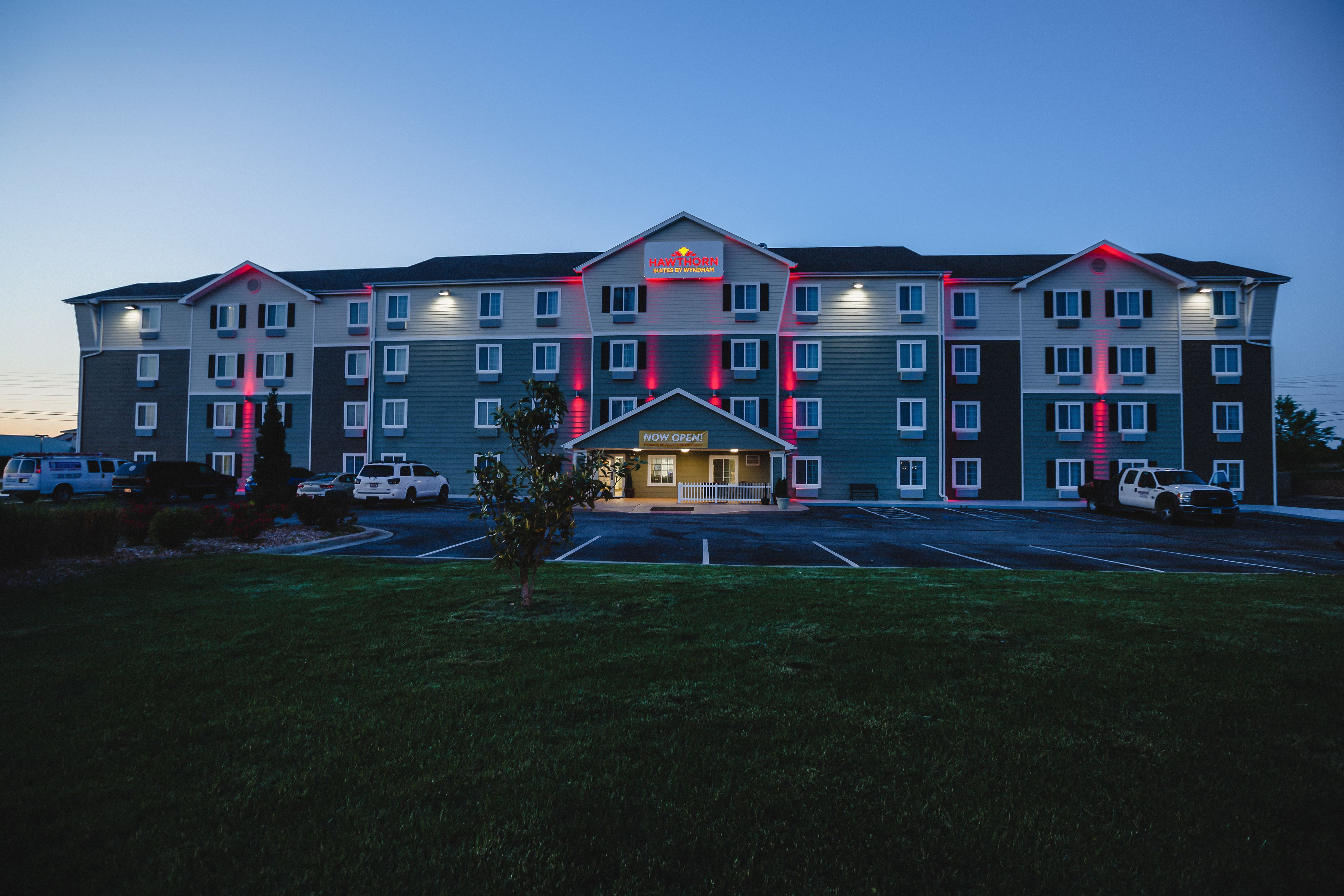 A multi-story hotel with a prominent entrance, a parking lot, and a small lawn area in front.