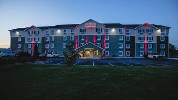 A multi-story hotel with a prominent entrance, a parking lot, and a small lawn area in front.