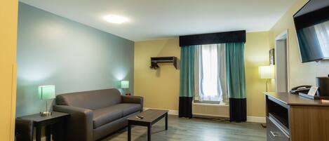A compact living room with a sofa, a coffee table, a desk with a telephone, and a flat-screen TV mounted on the wall.