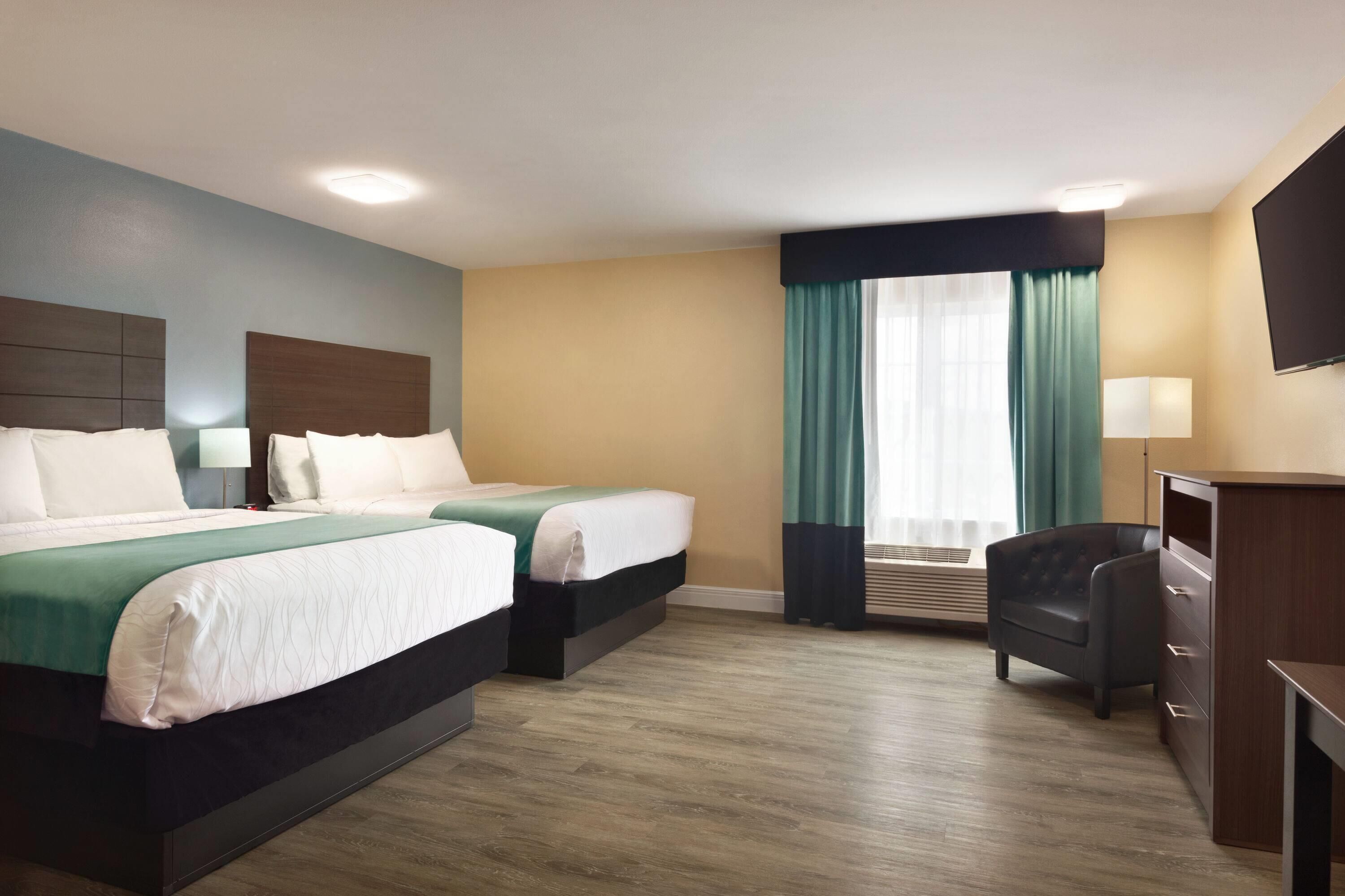 A hotel room with two beds, a desk, a chair, a TV, and a window with curtains.