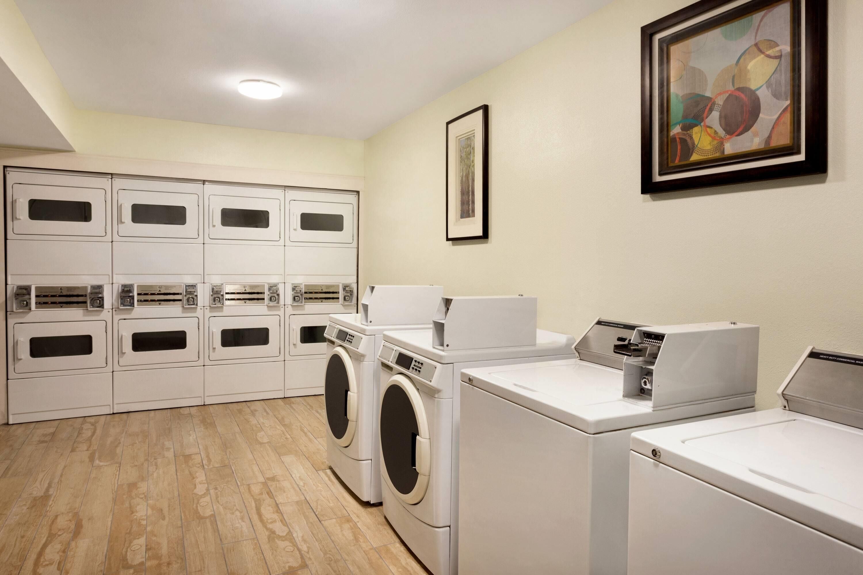 A laundry room with multiple washing machines and dryers, a tiled floor, and a framed artwork on the wall.