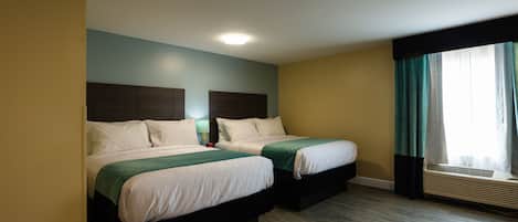 A hotel room with two beds, a ceiling light, an air conditioning unit, and a window with curtains.