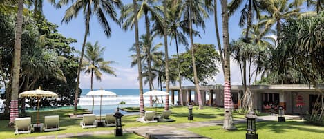 A resort with a pool, lounge chairs, palm trees, and a view of the ocean.