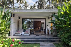 Uma casa moderna com entrada coberta, área de estar com sofá e almofadas, e uma grande planta em vaso.