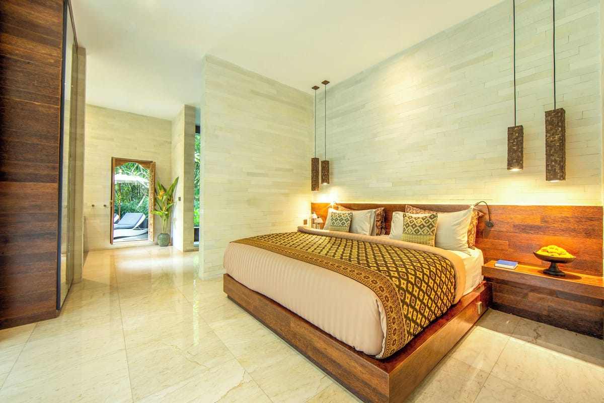 A modern bedroom with a large bed, wooden headboard, and pendant lighting.