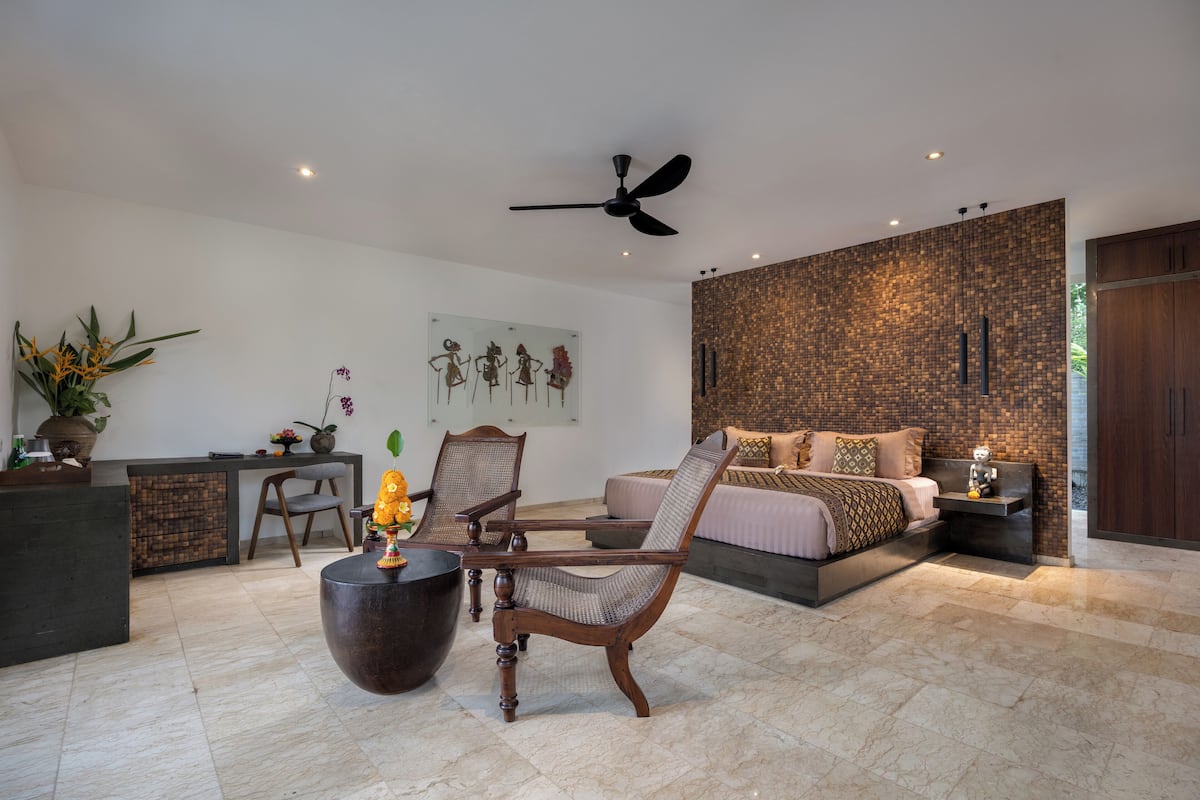 A modern bedroom with a bed, a desk, a chair, and a ceiling fan.
