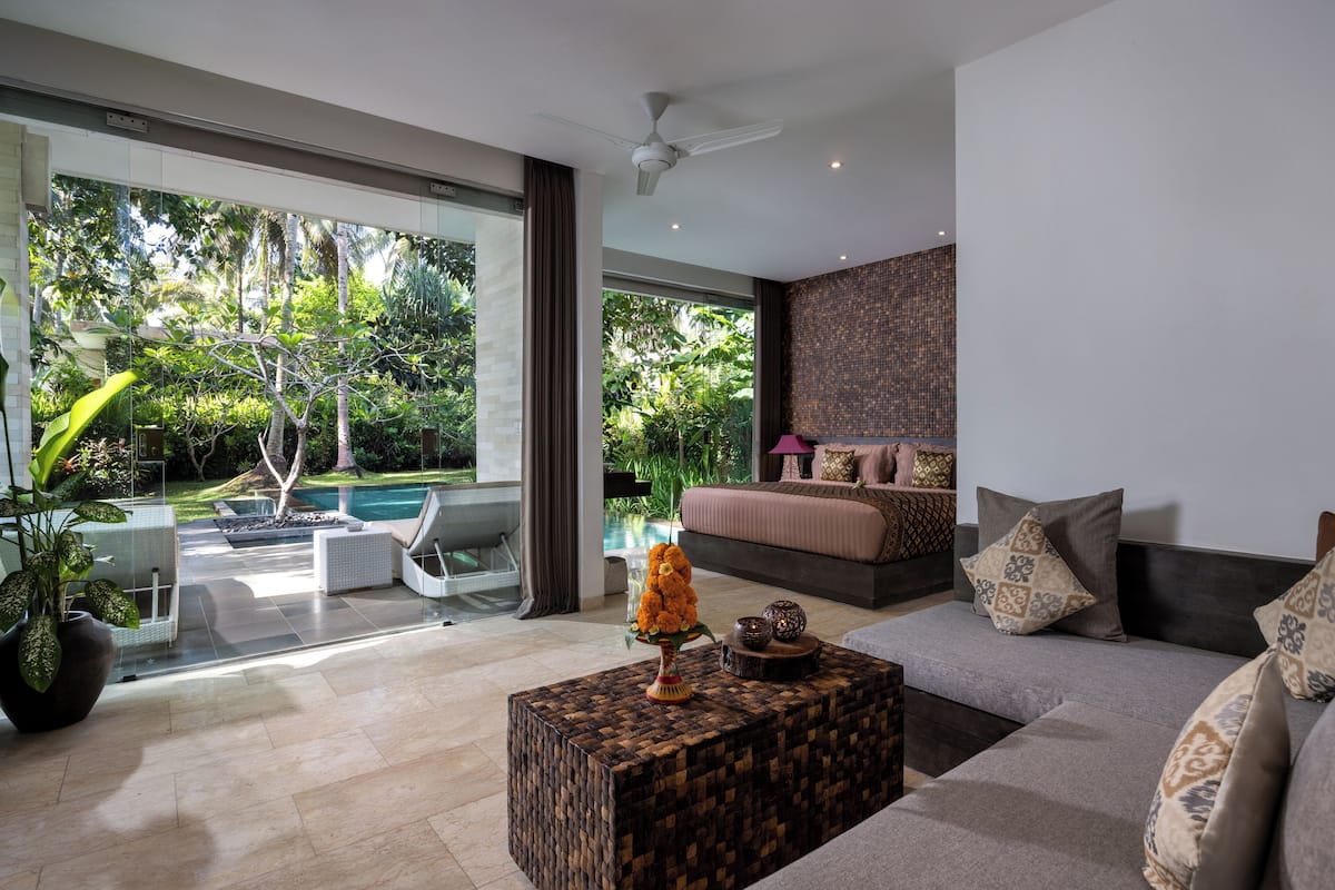 A modern living room with a large window, a sofa, a coffee table, and a view of a pool and garden.