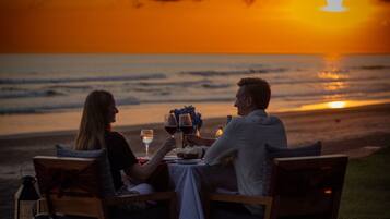 Una pareja cenando en una mesa con vistas a la puesta de sol sobre el océano.