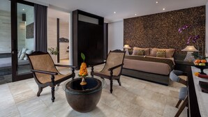 Una habitación de hotel moderna con una cama grande, dos sillones, una mesa de centro con un jarrón y una pared con textura.