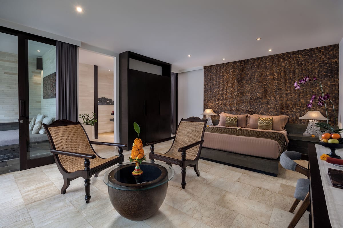 A modern hotel room with a large bed, two armchairs, a coffee table with a vase, and a textured wall.