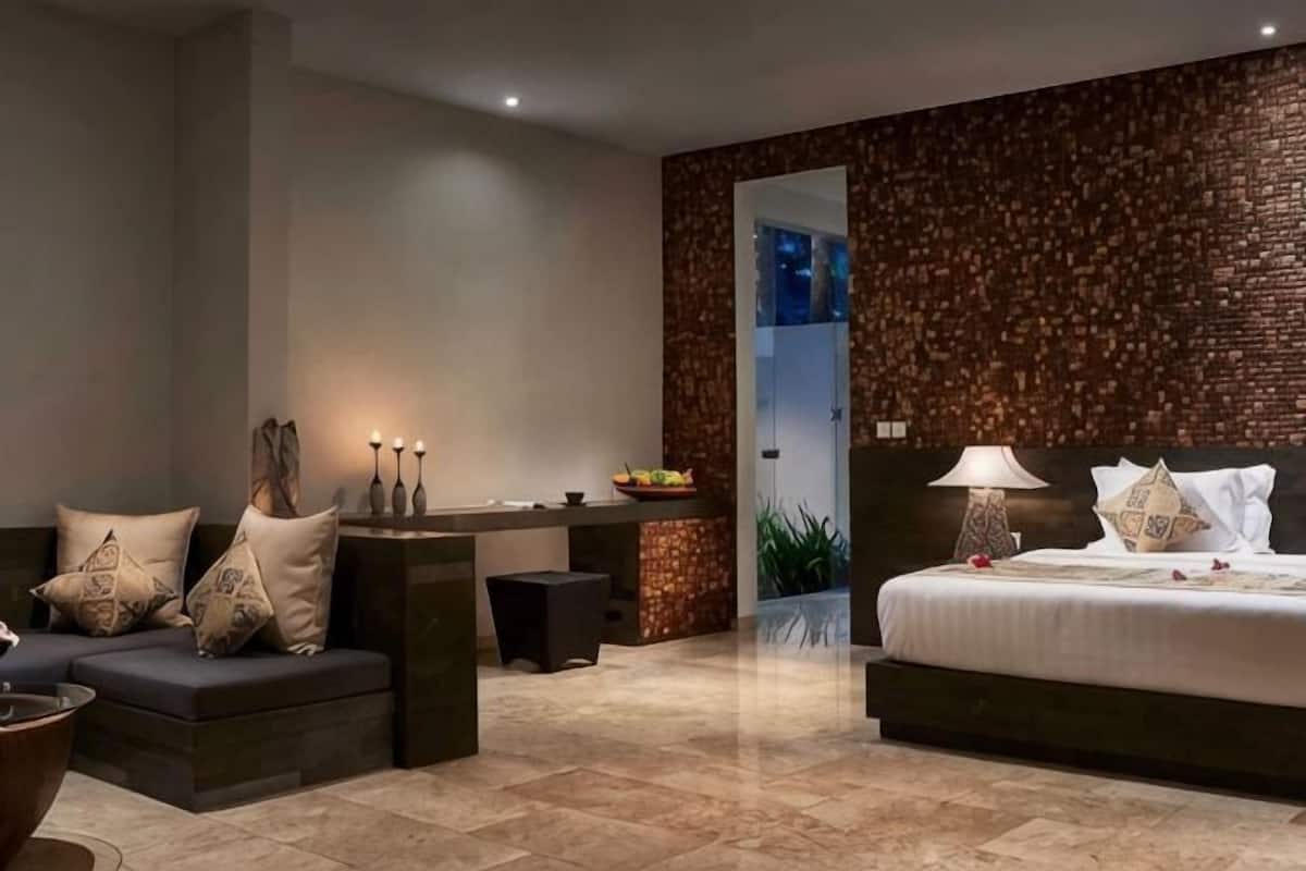 A modern hotel room with a sofa, a bedside table with candles, a bed with a headboard, and a decorative wall.