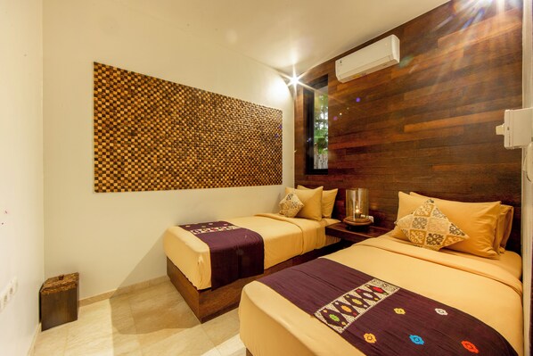 Une chambre d’hôtel avec deux lits, une décoration murale à motifs à carreaux, une tête de lit en bois et une table de chevet avec une lampe.