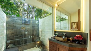 Un baño moderno con ducha envuelta en vidrio, un espejo grande y un tocador de madera.