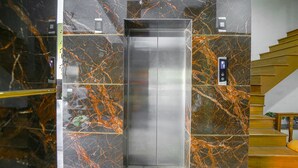 Un ascensor con detalles metálicos, rodeado de paredes de mármol con vetas anaranjadas.