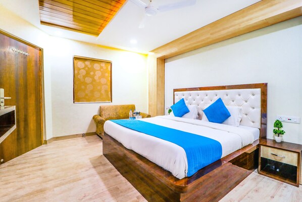 A well-lit bedroom with a large bed, wooden flooring, a headboard with blue pillows, and a small bedside table with a plant. - Hotel City Castle (Amritsar)