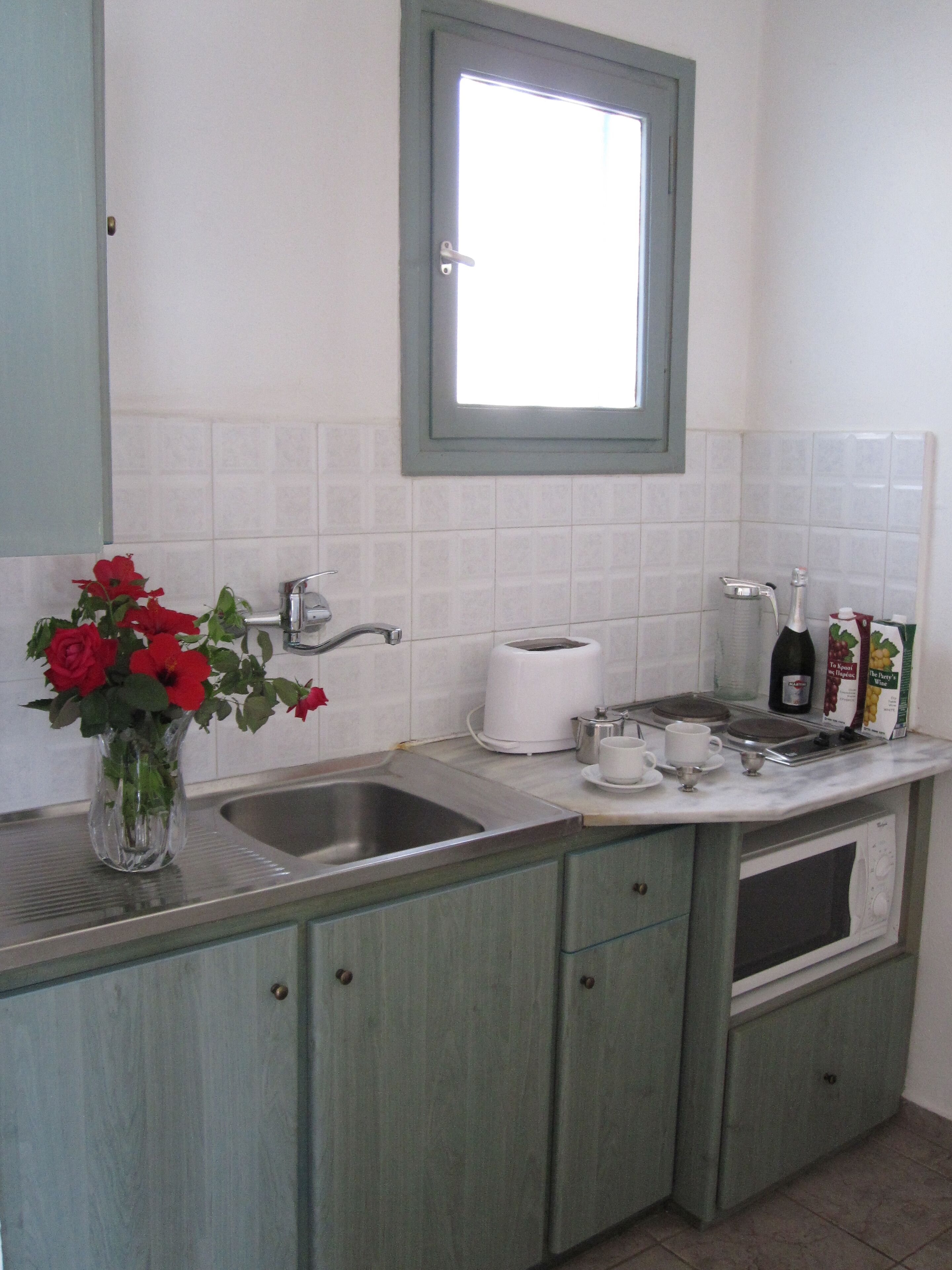 A kitchen with a sink, a toaster, a wine bottle, and a vase with red flowers.