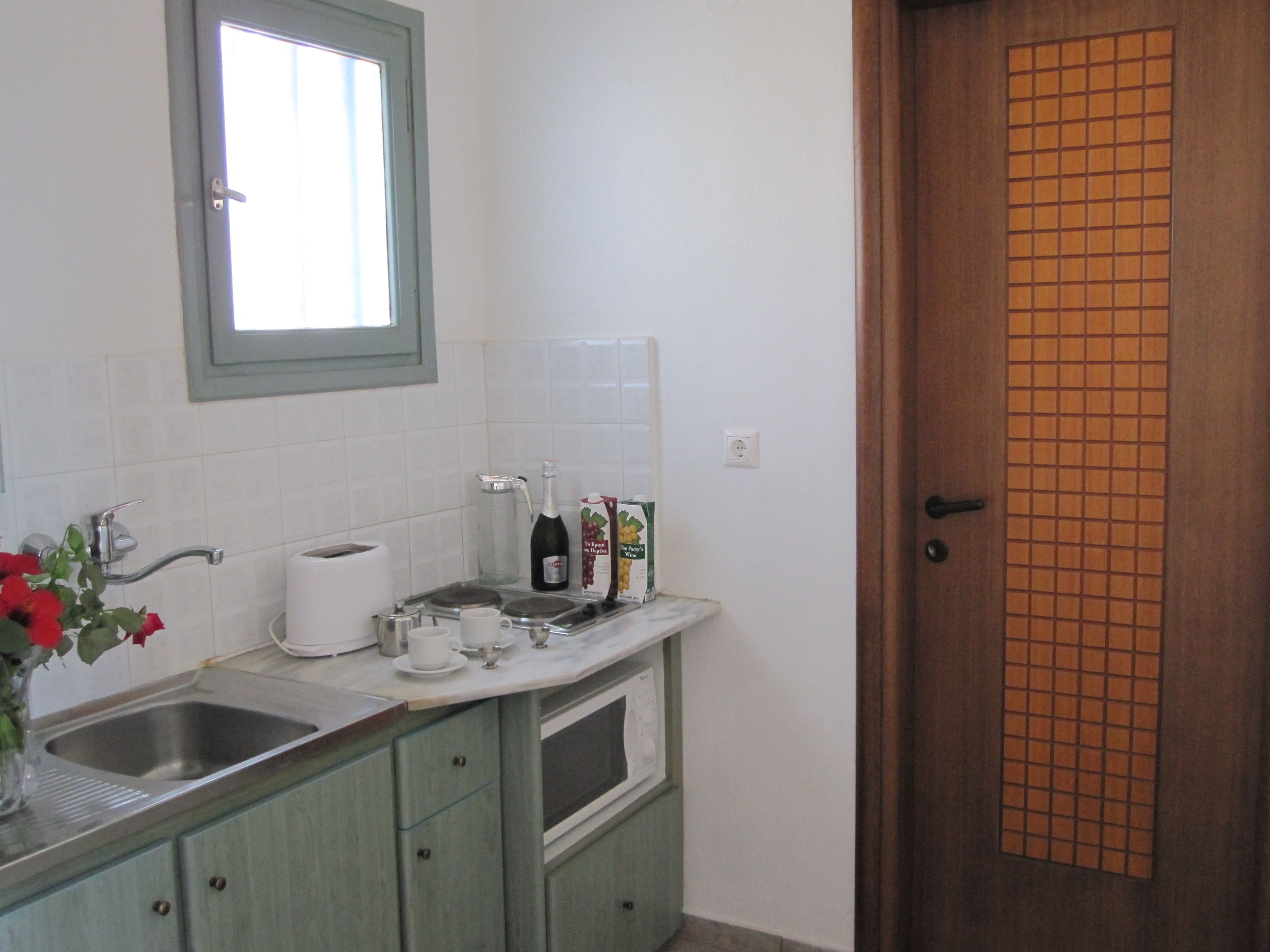 A kitchen with a sink, a window, a door, and a countertop with a bottle and a box.