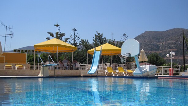 A swimming pool with a slide and sun umbrellas, surrounded by lounge chairs and a mountain backdrop.