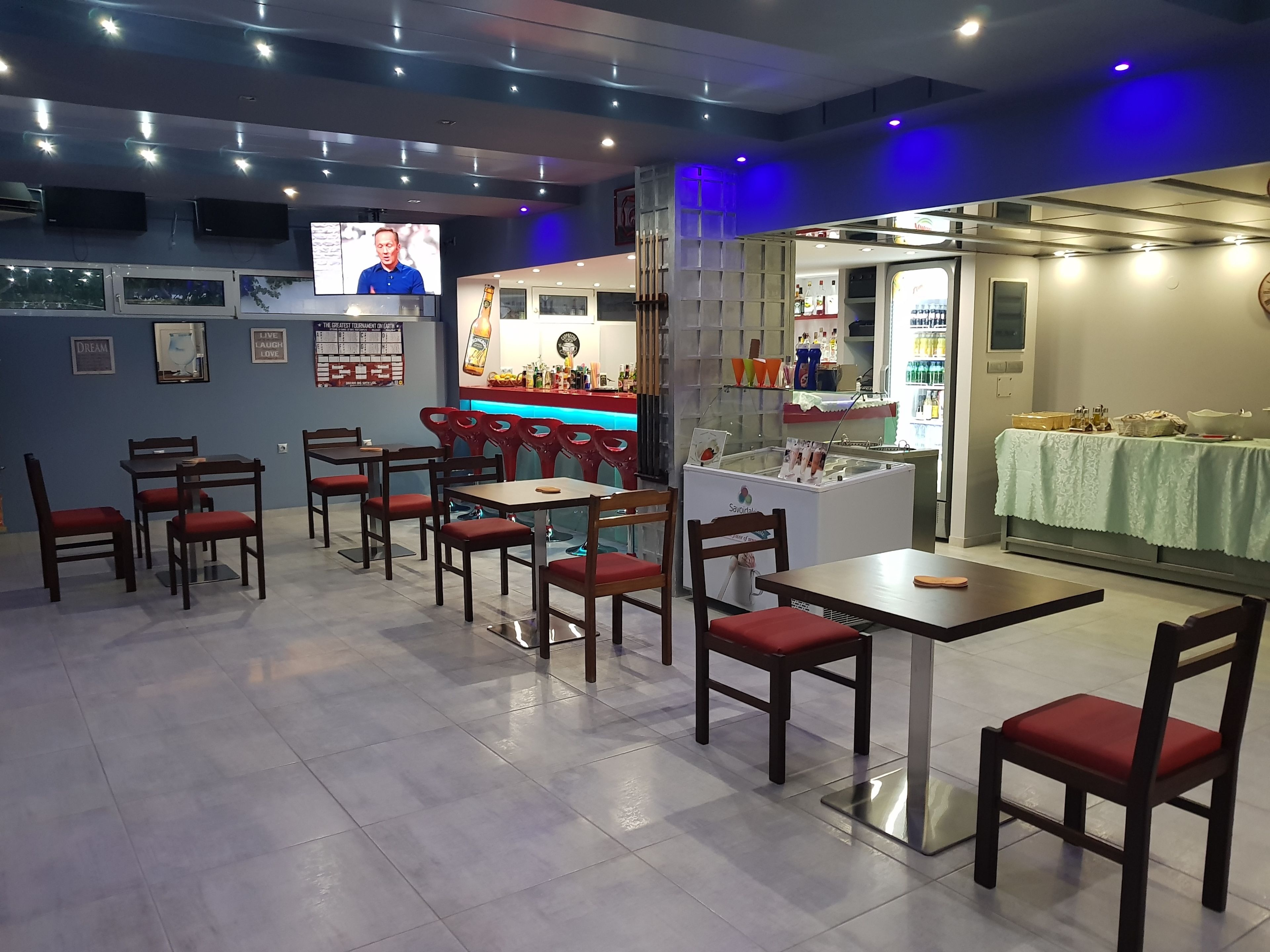 A restaurant with multiple tables and chairs, a bar area, and a television screen.