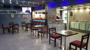 A restaurant with multiple tables and chairs, a bar area, and a television screen.