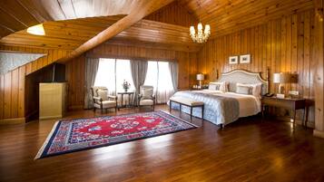 Um quarto amplo com uma cama grande, um lustre, paredes de madeira e um tapete vermelho estampado.