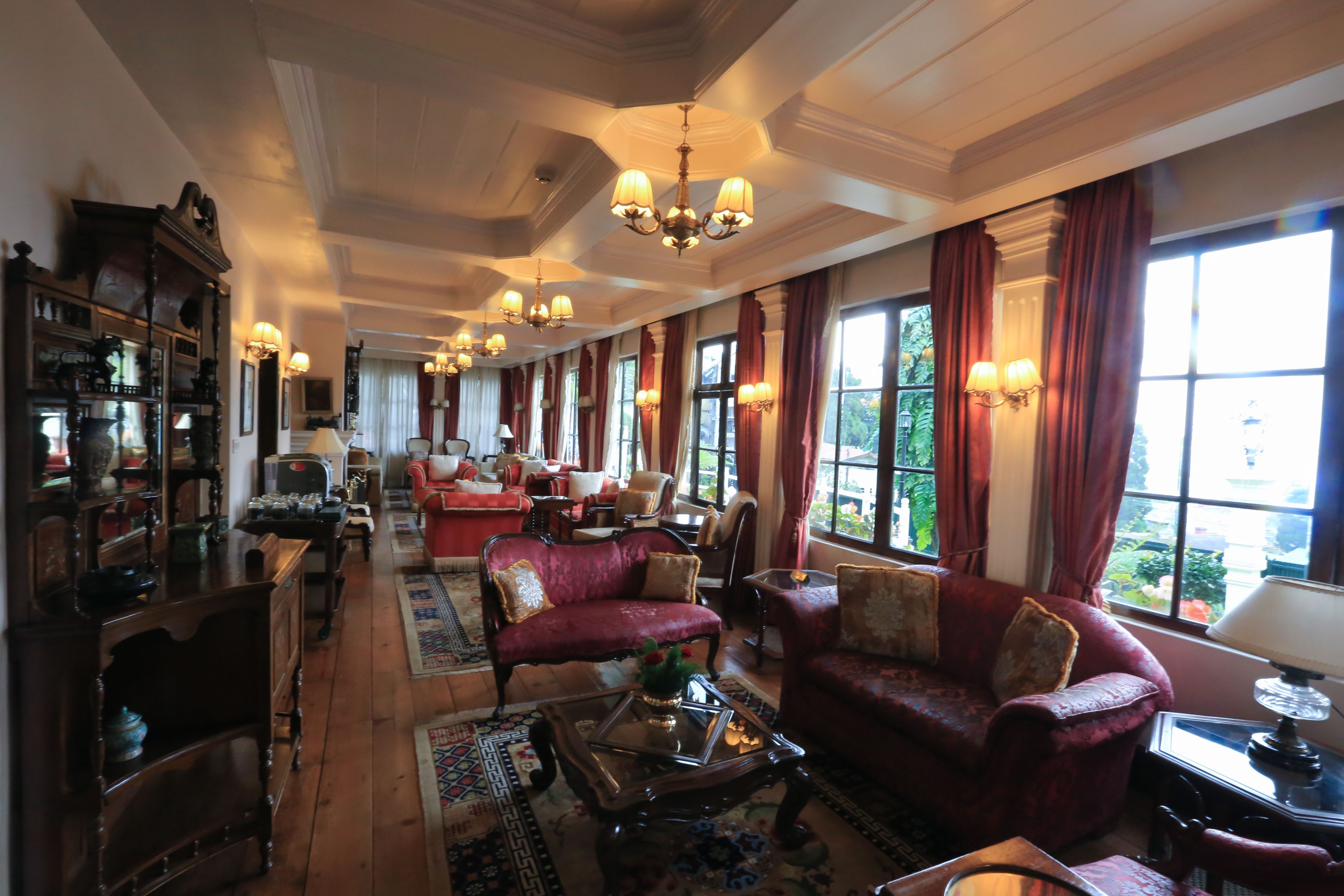 A spacious living room with red sofas, a wooden coffee table, and a large window with curtains.