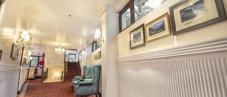 A hallway with a red carpet, blue upholstered chairs, and framed pictures on the wall.