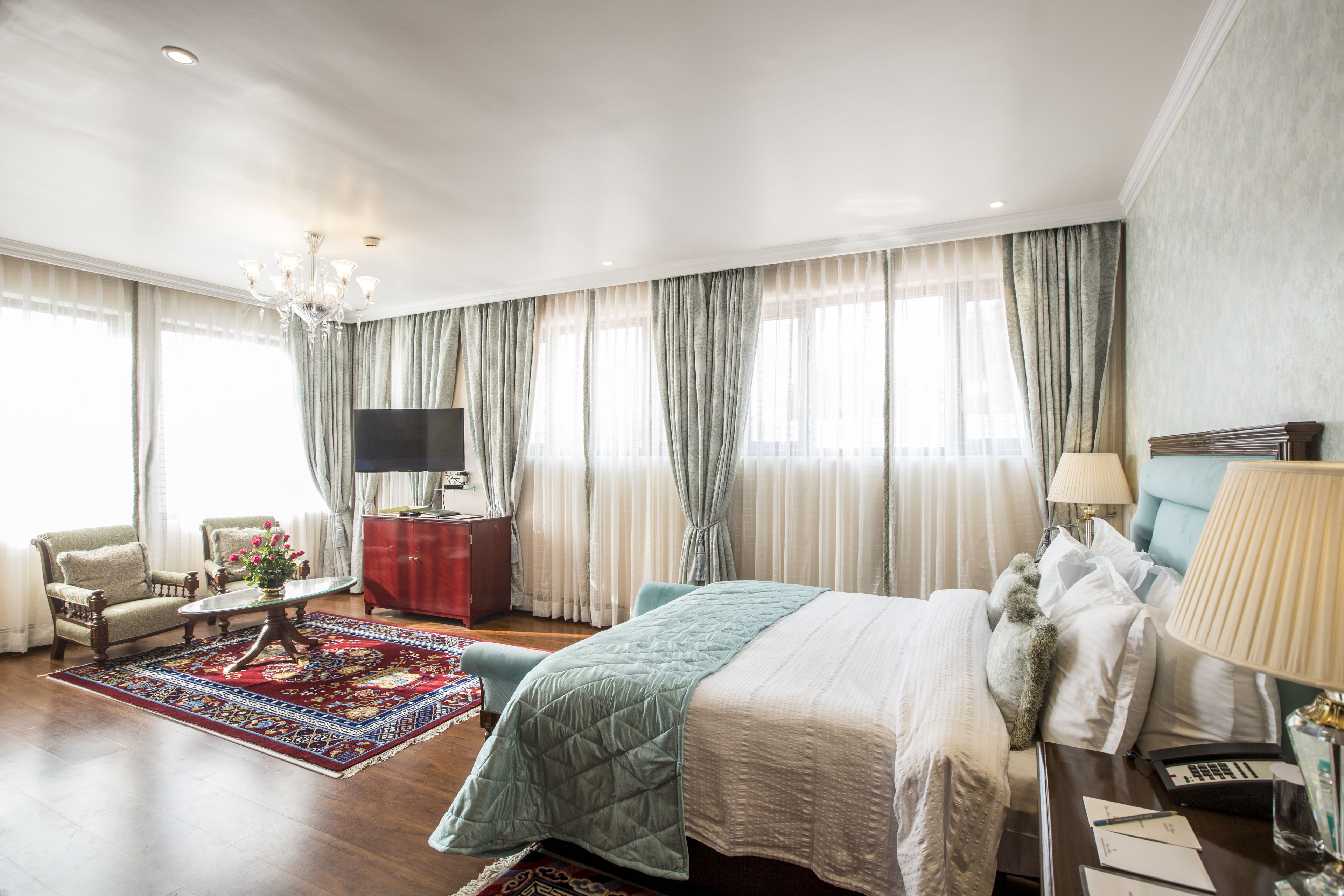 Un'ampia camera d'hotel con un letto grande, una zona salotto con una poltrona e un tavolino, una televisione e una scrivania con una lampada.