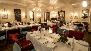 Un comedor formal con varias mesas dispuestas para el servicio, elegantes lámparas de araña y decoración clásica.