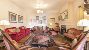 A spacious living room with a large red sofa, two armchairs, a patterned rug, and a fireplace.