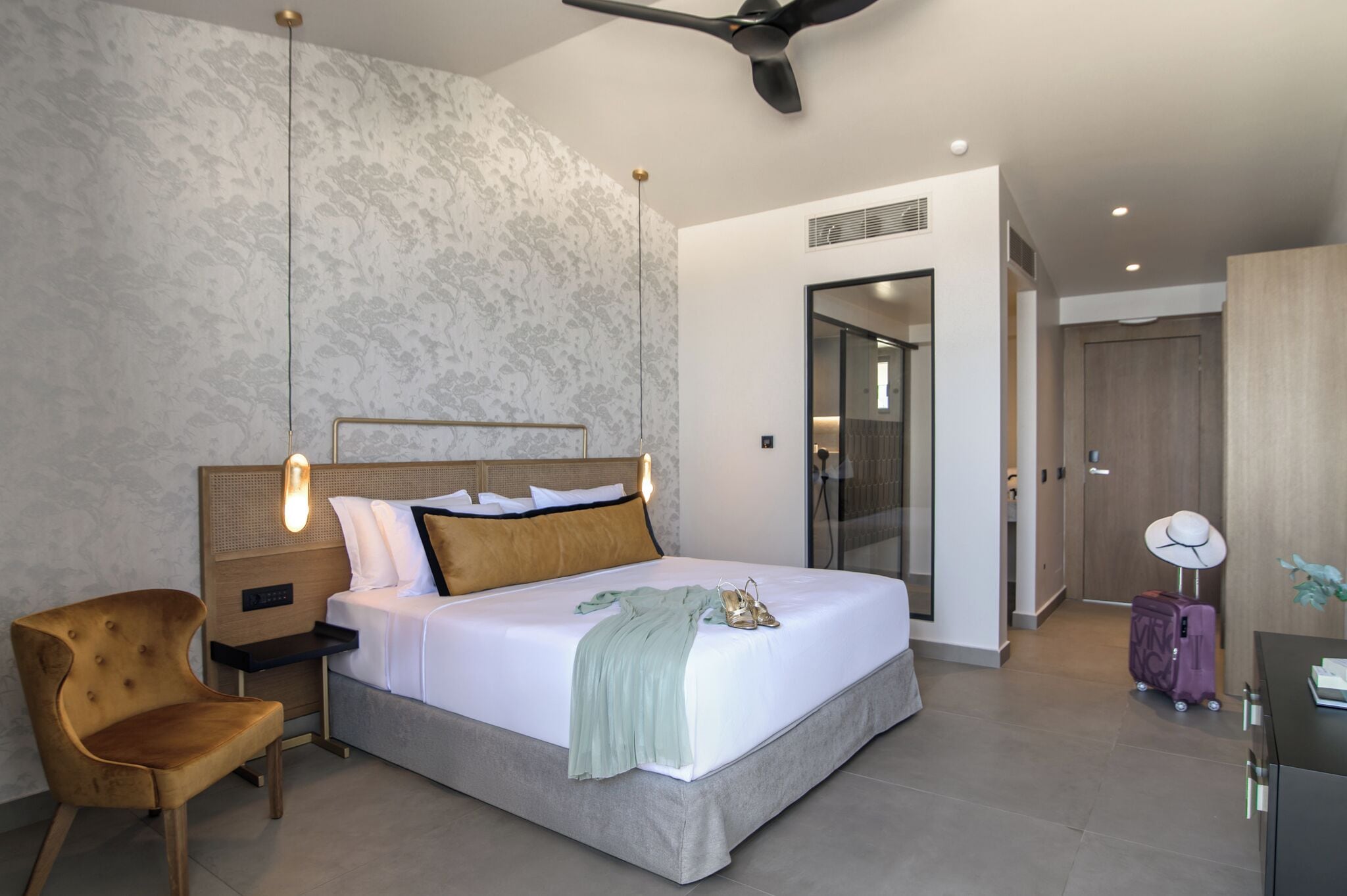 Una habitación de hotel moderna con una cama grande, una mesita de noche de madera, una silla, una maleta y un ventilador de techo.