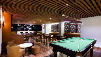 Una sala de billar con mesa de pool, zona de estar y bar.