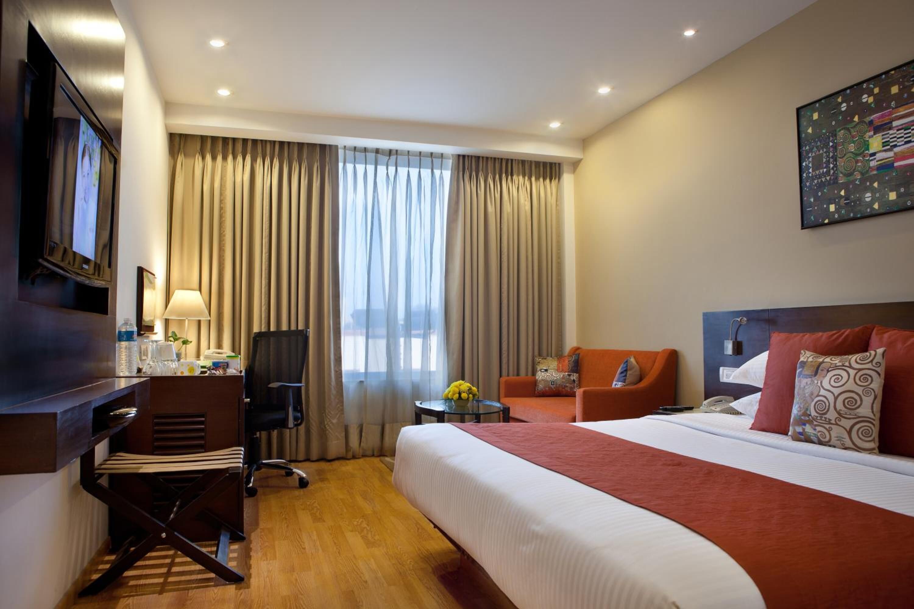 A hotel room with a large bed, a desk with a chair, a sofa, and a TV.