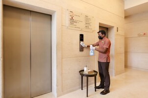 A person disinfecting an elevator button with a spray bottle and a cloth.