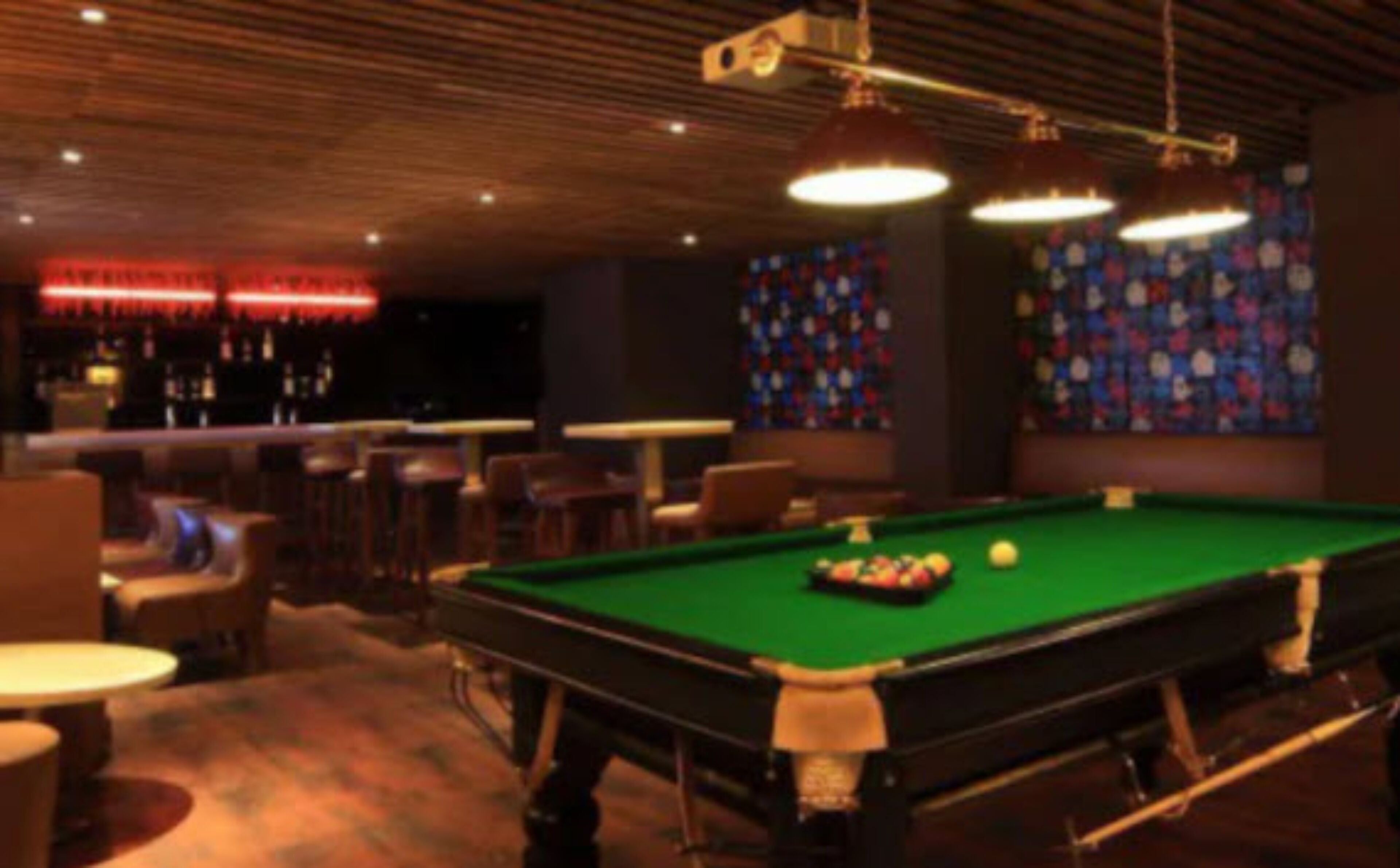 Un tavolo da biliardo con le palle, un'area bar con sgabelli e un muro decorato.