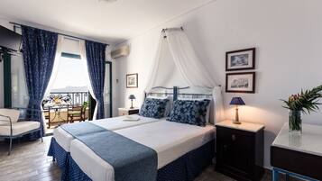 A hotel room with a large bed, a bedside table with a lamp, a small table with a chair, and a view of the outdoors.