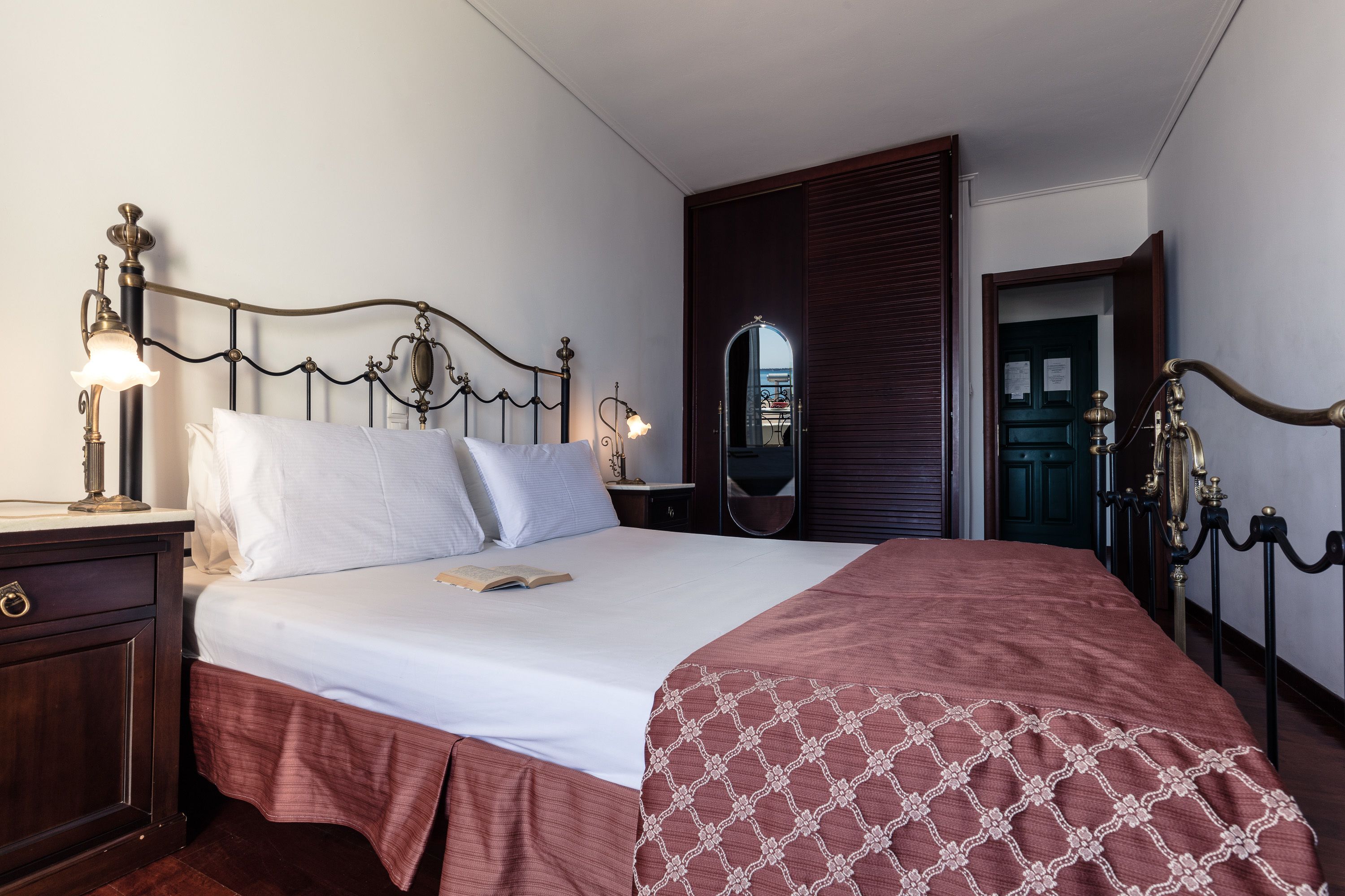 A neatly made bed with a patterned bedspread, a bedside table with a lamp, and a mirror on the wall.