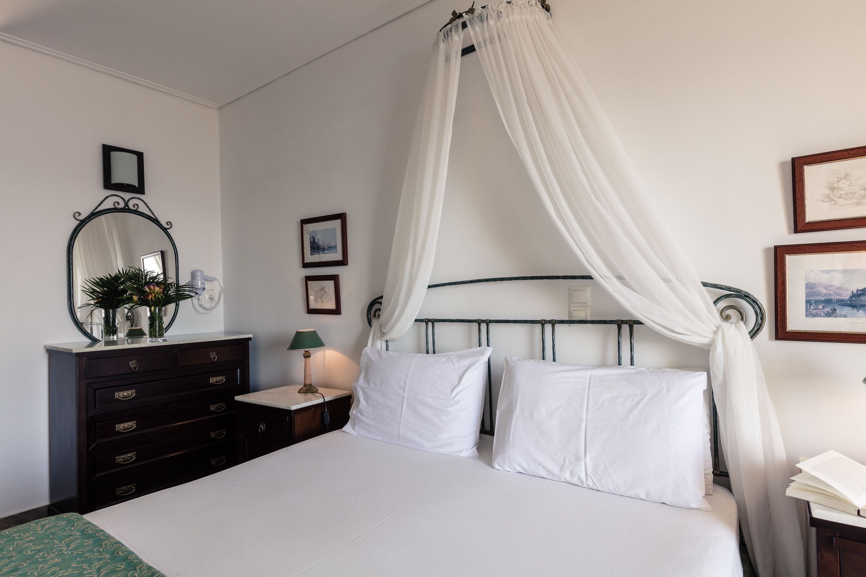A bedroom with a bed, a nightstand, a dresser, a mirror, and a canopy bed.
