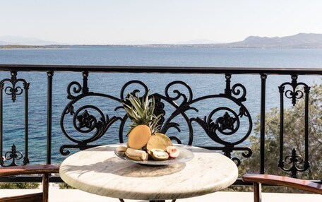 A round marble table with a fruit plate, a metal railing, and a view of the sea and mountains.