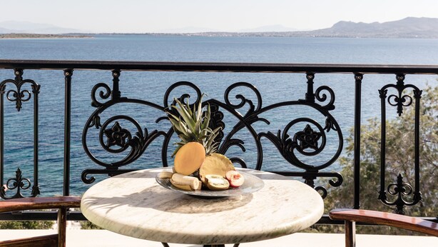 Ein runder Marmor-Tisch mit einer Obstplatte, einem Metallgeländer und Blick auf das Meer und die Berge.