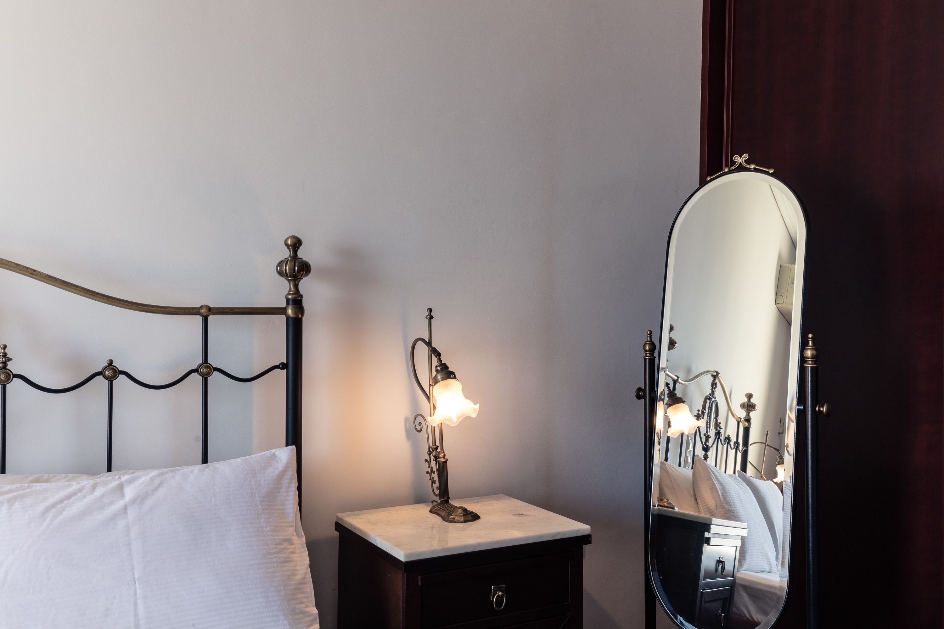 Un lit avec une tête de lit, une table de chevet avec une lampe et un miroir qui reflète la pièce.