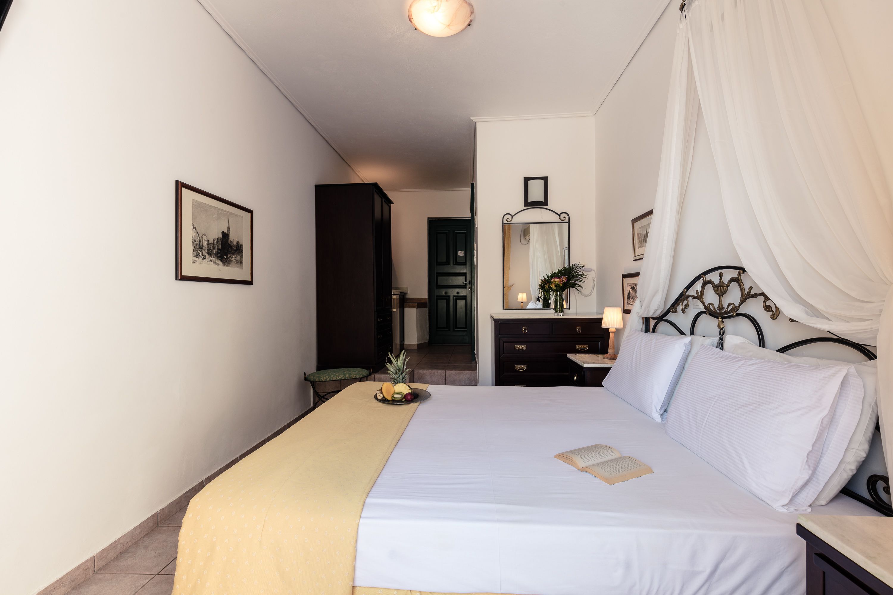 A neatly arranged bedroom with a bed, a bedside table with a lamp, a mirror, and a framed picture on the wall.