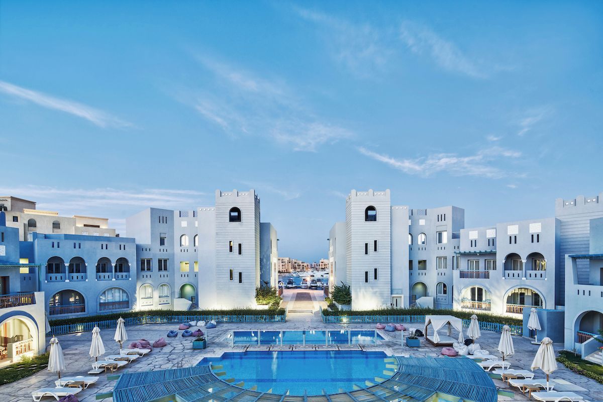 A resort with a central pool, lounge chairs, and a view of the city in the distance.