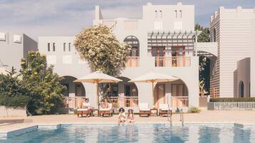 A pool area with lounge chairs and umbrellas, surrounded by a building with arched windows and balconies.