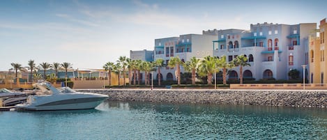 A marina with a yacht docked, a stone wall, and a building with multiple balconies and arches.