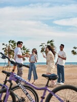 Un gruppo di persone su una spiaggia, con biciclette in primo piano.