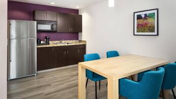 Une cuisine moderne avec des meubles de couleur sombre, un réfrigérateur en acier inoxydable, un four à micro-ondes et un comptoir en granit. On y trouve une table à manger en bois avec des chaises bleues.