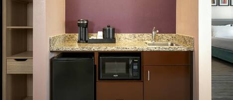 A compact kitchenette with a microwave, coffee maker, and sink.