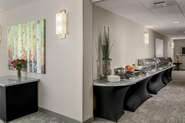 A modern hotel lobby with a buffet setup, a large abstract painting, and a vase with flowers. - Hilton Garden Inn Eugene/Springfield (Springfield)