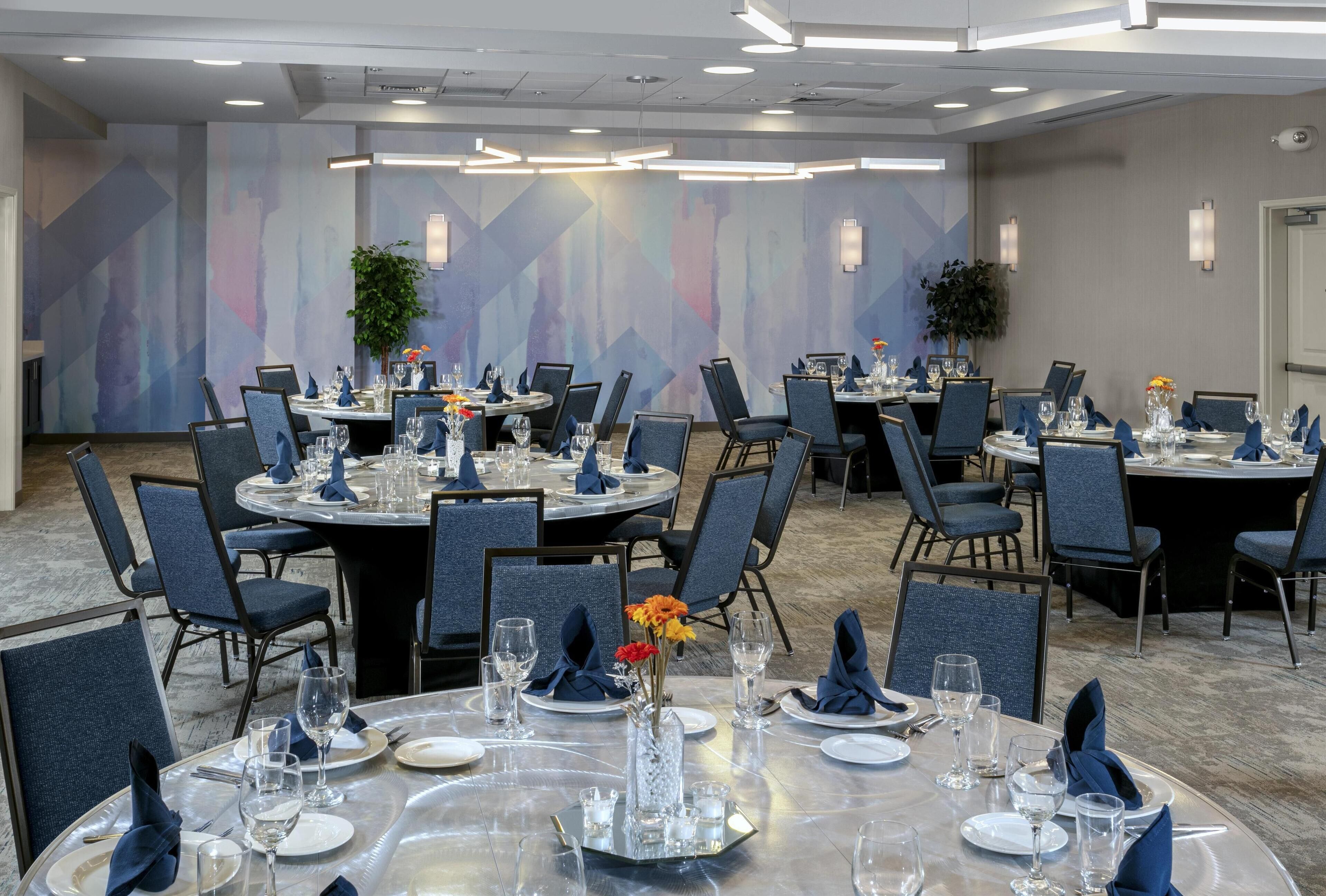 A conference room with round tables, blue chairs, and a modern abstract wall design.